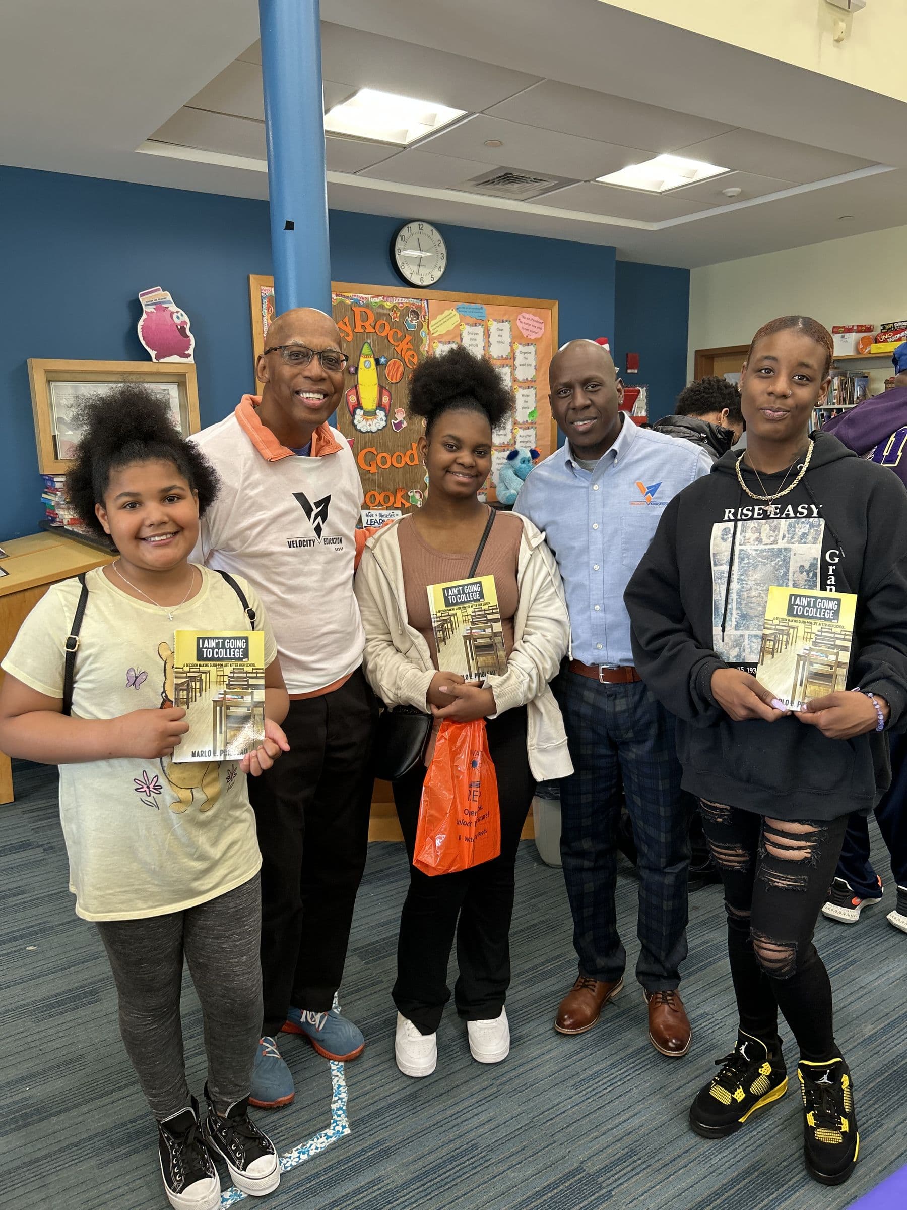 Velocity students holding copies of I Ain't Going to College alongside Marlo Prioleau and a program partner