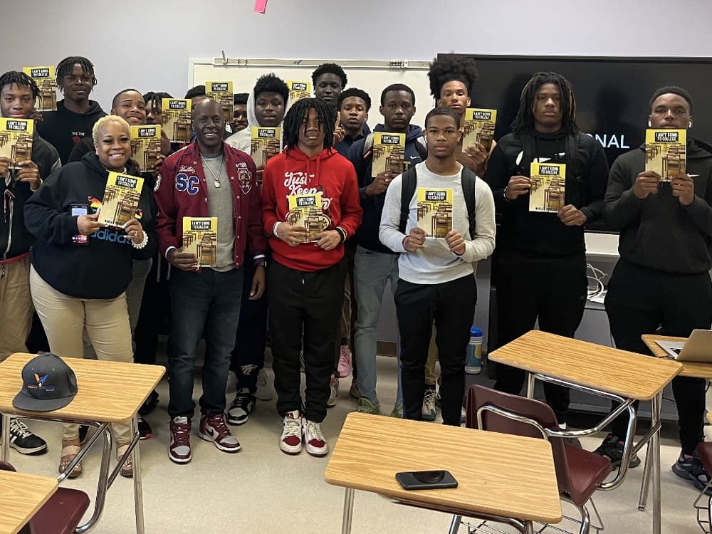 A full class of students holding Velocity's student book with Marlo Prioleau and their teacher